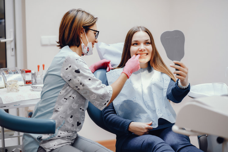 a patient is looking at her smile in a mirror, with her cosmetic dentist next to her.